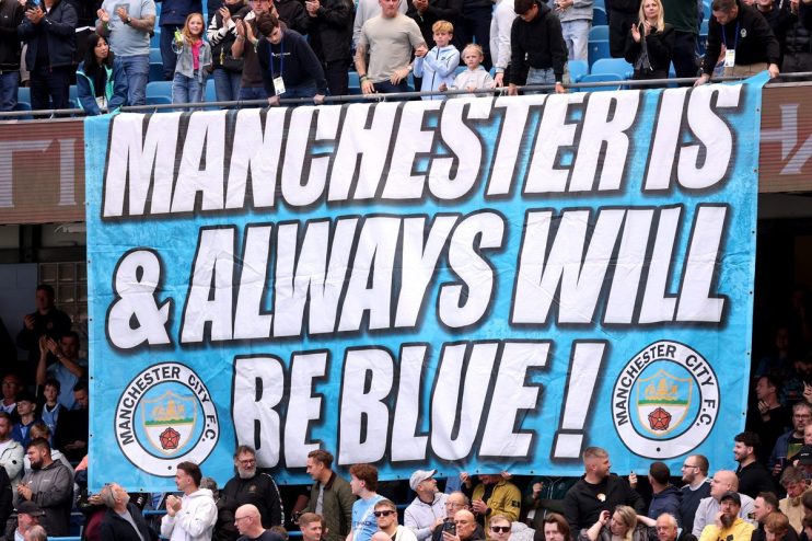A large banner reads Manchester Is & Always Will Be Blue! with Manchester City F.C. crests, surrounded by cheering fans.