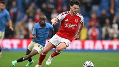 Declan Rice of Arsenal dribbles the football during a match, with another player in blue closely behind him.