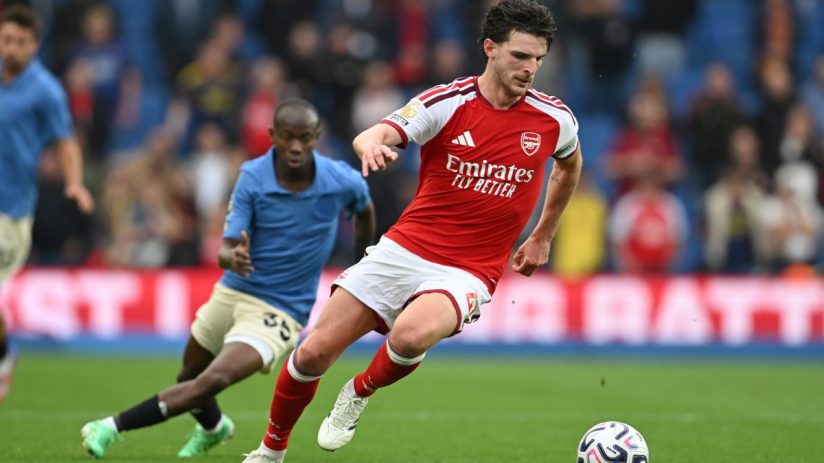 Declan Rice of Arsenal dribbles the football during a match, with another player in blue closely behind him.