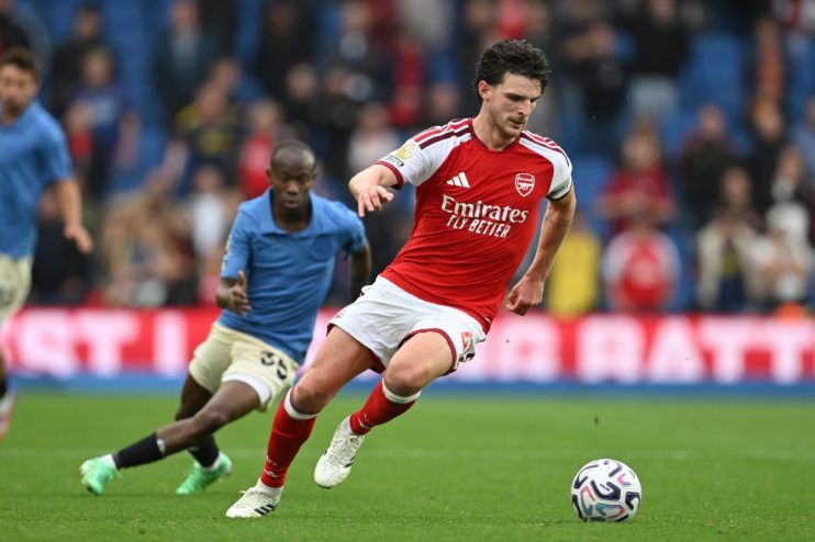 Declan Rice of Arsenal dribbles the football during a match, with another player in blue closely behind him.