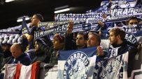 Sports fans in a stadium holding up scarves and flags for Bordeaux