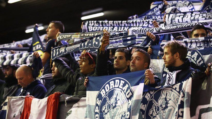 Sports fans in a stadium holding up scarves and flags for Bordeaux