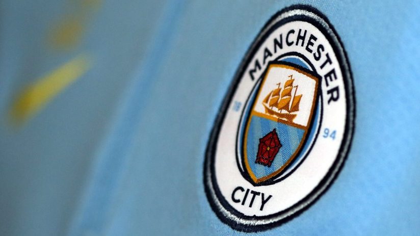 Close-up of the Manchester City football club crest on a light blue jersey.