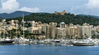 Palma de Mallorca harbor with yachts, city buildings, and Bellver Castle on a forested hill