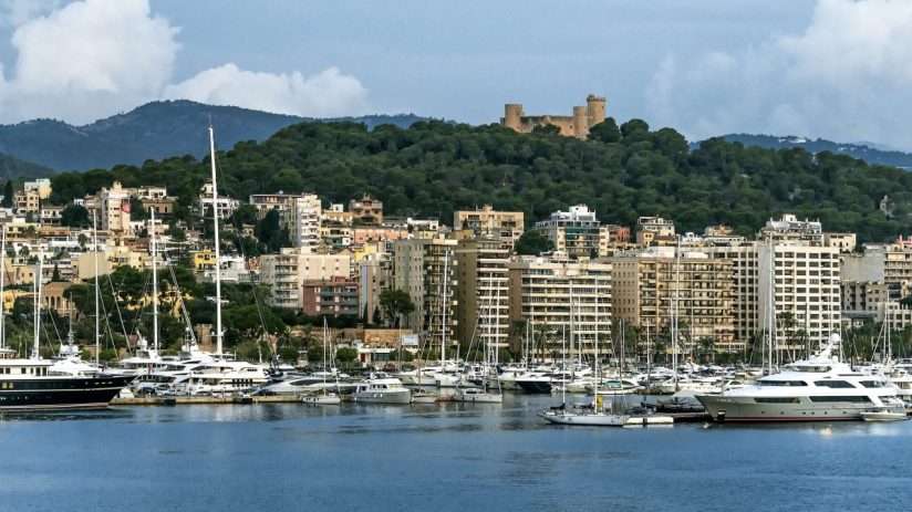 Palma de Mallorca harbor with yachts, city buildings, and Bellver Castle on a forested hill