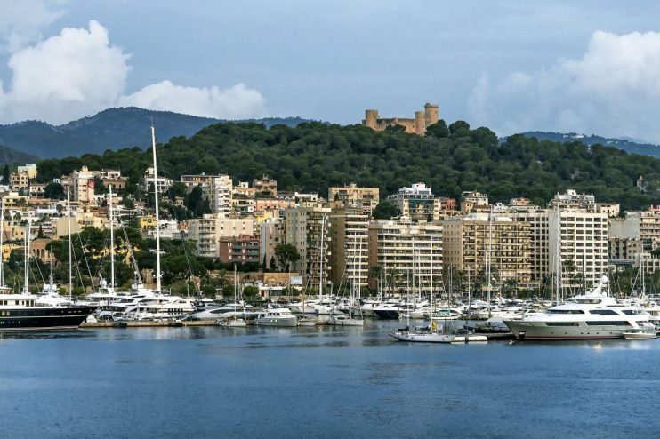 Palma de Mallorca harbor with yachts, city buildings, and Bellver Castle on a forested hill