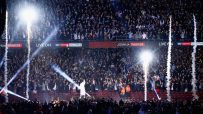 Crowd cheers with phone lights, pyrotechnics, and a performer on stage under Joshua Parker and Sky Sports Box Office signs.