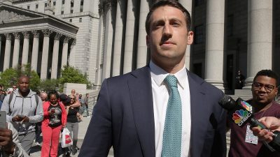 Man in a suit and tie speaks into a CNBC microphone outside a courthouse with large columns.