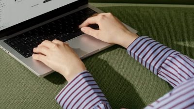 Hands typing on a laptop keyboard with a business application visible on screen, on a green textured surface.