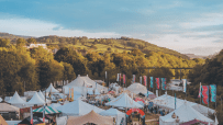 Overview of the How The Light Gets In festival with numerous white tents and banners in a valley by a river