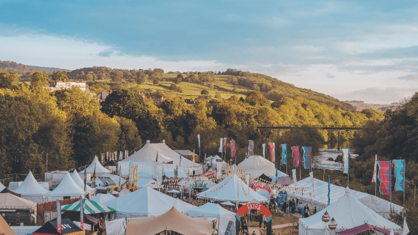 Overview of the How The Light Gets In festival with numerous white tents and banners in a valley by a river