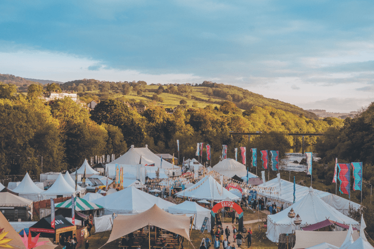Overview of the How The Light Gets In festival with numerous white tents and banners in a valley by a river