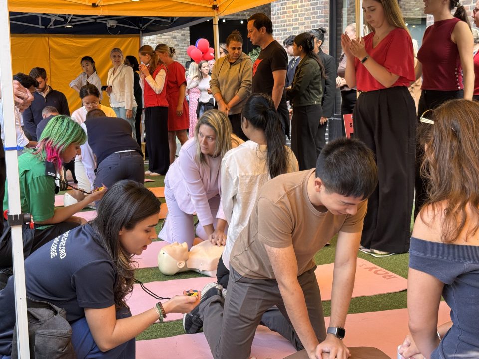 Attendees learning CPR with mannequins and instructors under a yellow tent.