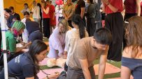 People practicing CPR on mannequins during a training session under a yellow canopy
