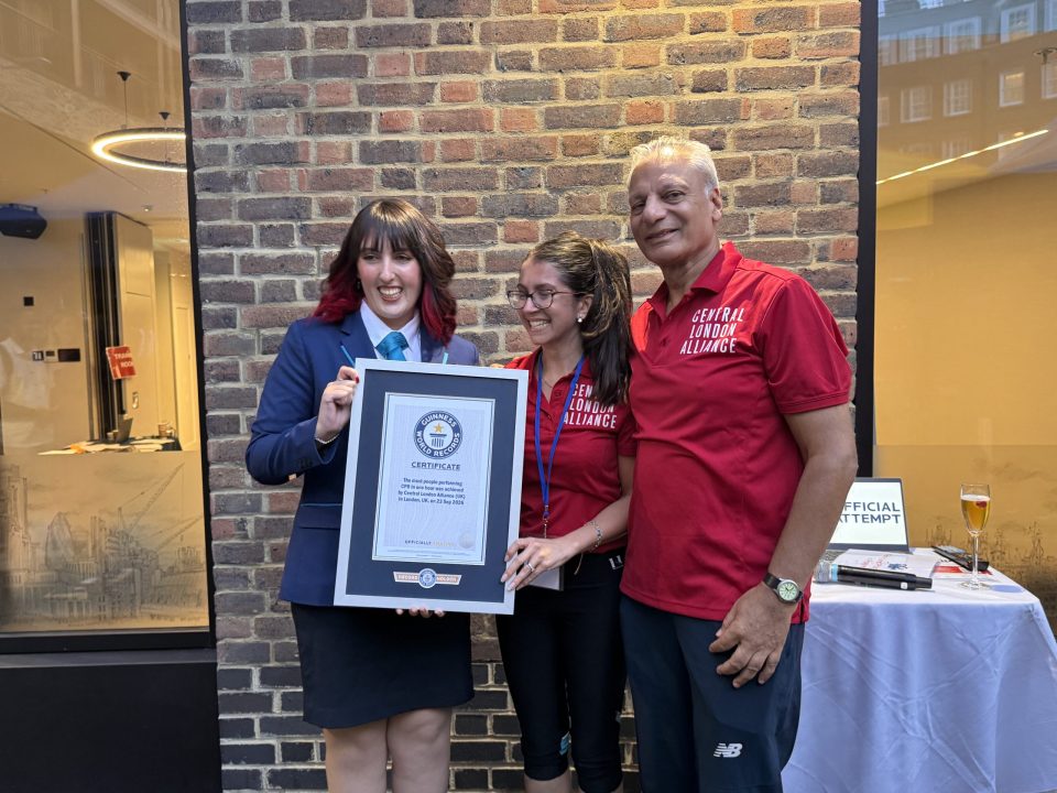 Three people, two women and one man, holding a framed Guinness World Records certificate for CPR achievement.