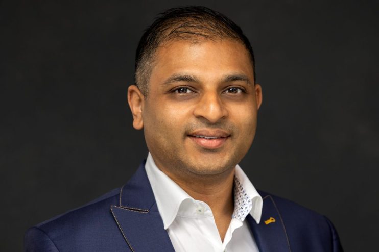 Ian Ferrao, business executive, wearing a blue suit and white shirt, smiling against a dark background