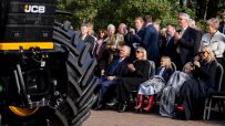 Audience observing a JCB machine, with a large tire prominent in the foreground.