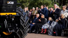 Audience observing a JCB machine, with a large tire prominent in the foreground.