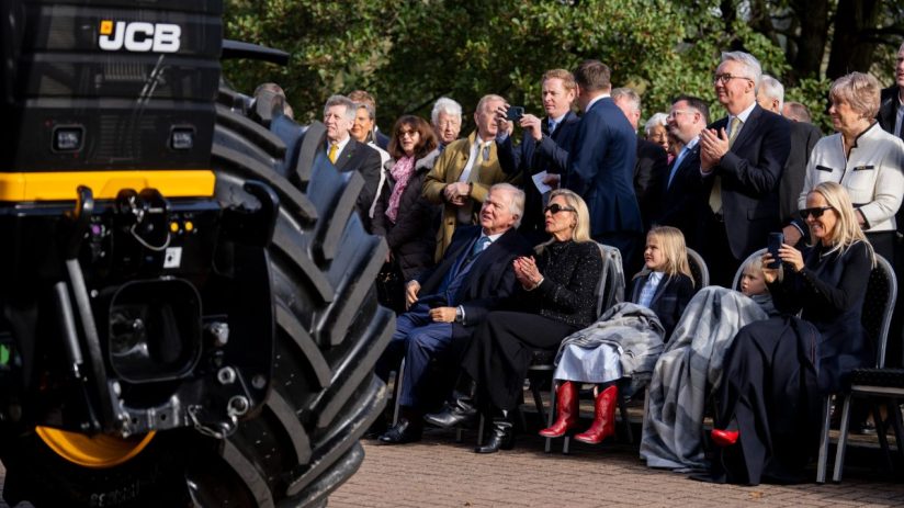Audience observing a JCB machine, with a large tire prominent in the foreground.