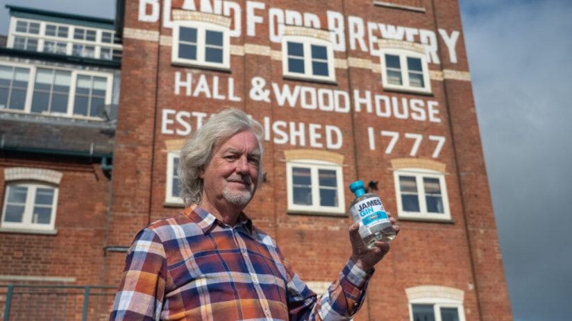 James May holding a bottle of James Gin in front of Blandford Brewery, Hall & Woodhouse established 1777.