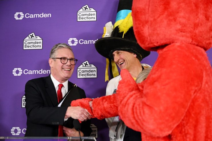 Keir Starmer shaking hands with a man in a tall hat and red furry costume at a Holborn and St Pancras election event.