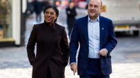 Kemi Badenoch and Andrew Griffith walking together on a city street, smiling.