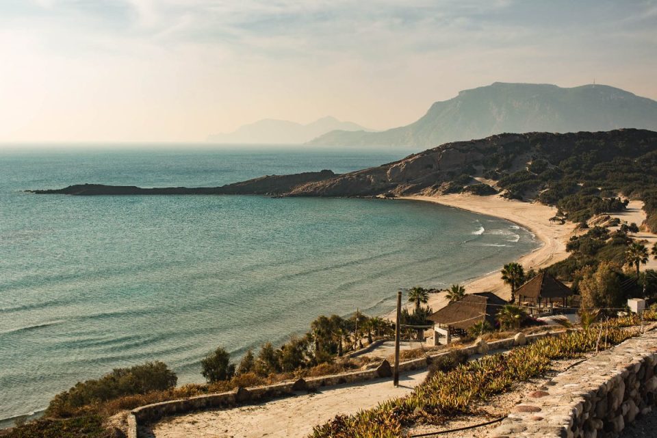 Scenic Kos beach with clear turquoise waters, sandy shore, and distant mountains. Ideal for Kos hotels.