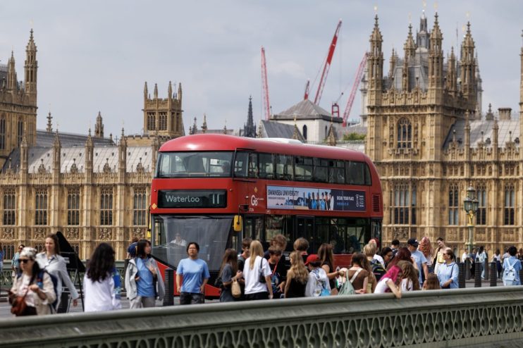 London red double-decker bus with Waterloo destination sign, driving past the Houses of Parliament.