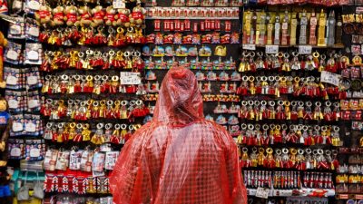 Person in red poncho browsing a stall filled with London tourist keyrings and souvenirs like magnets and teddy bears.