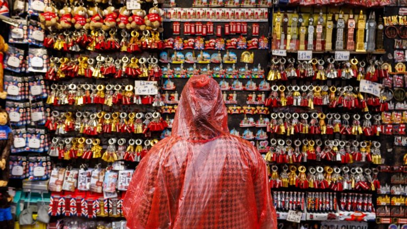 Person in red poncho browsing a stall filled with London tourist keyrings and souvenirs like magnets and teddy bears.