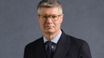 Lord Wolfson, CEO of Next Plc, wearing a dark suit, light blue shirt, and spotted tie