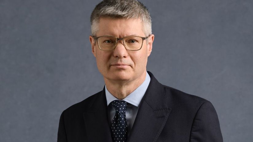 Lord Wolfson, CEO of Next Plc, wearing a dark suit, light blue shirt, and spotted tie