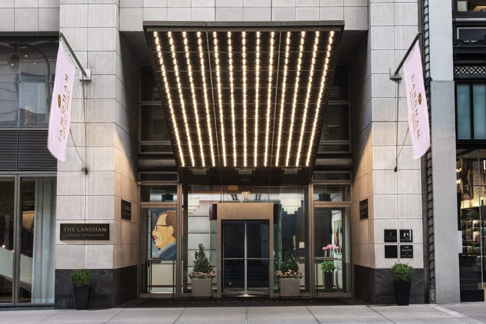 The Langham Hotel New York entrance on Fifth Avenue with illuminated awning and branded flags.