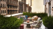Rooftop terrace of a New York hotel with lush greenery, comfortable seating, and city buildings in the background.