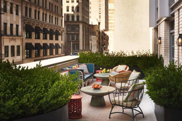 Rooftop terrace of a New York hotel with lush greenery, comfortable seating, and city buildings in the background.