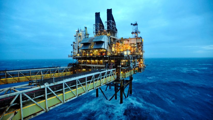 Offshore oil rig platform with illuminated facilities and a long gangway over choppy North Sea waters.