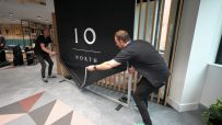Two men setting up a black banner with 10 NORTH in white text on a grey patterned carpet.