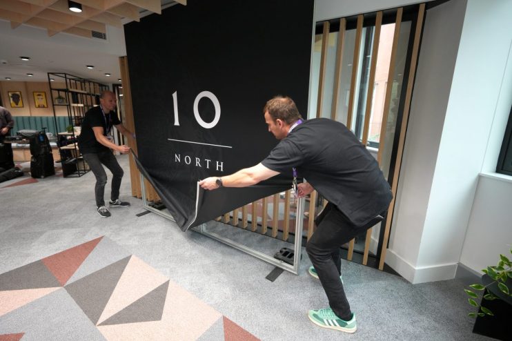 Two men setting up a black banner with 10 NORTH in white text on a grey patterned carpet.