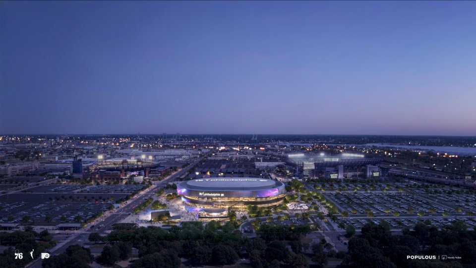 Aerial view of a modern sports arena in Philadelphia at dusk, surrounded by city lights and parking lots.
