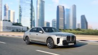Silver 2023 BMW 7 Series sedan driving on a city road with modern skyscrapers in the background