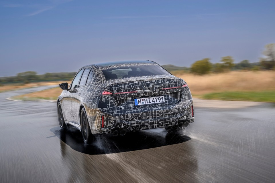Camouflaged BMW M5 prototype driving on a wet track, rear view, motion blur, performance testing.