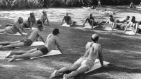 Men in swim trunks practicing yoga in a park, performing cobra pose on mats.