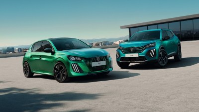 Green Peugeot 208 hatchback and teal Peugeot 2008 SUV parked on a rooftop lot with city views.