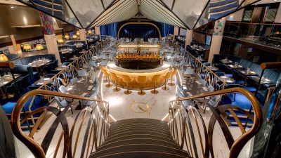 Elegant interior of Quaglinos London restaurant, featuring a central bar, dining tables, and a grand staircase.