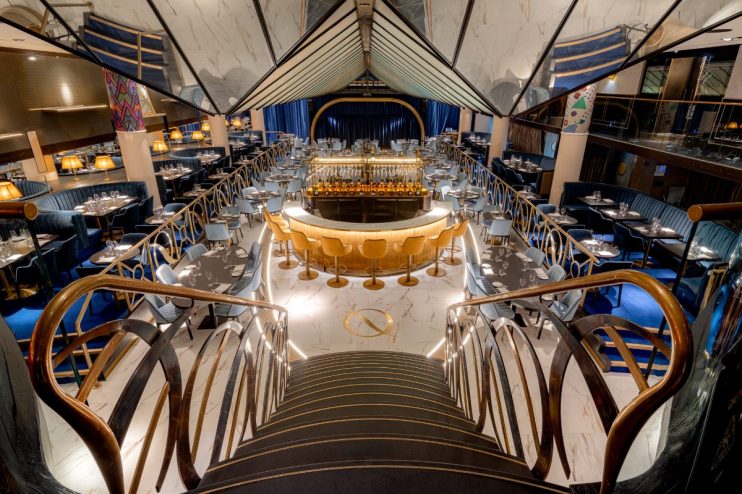 Elegant interior of Quaglinos London restaurant, featuring a central bar, dining tables, and a grand staircase.