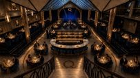 Elegant interior of Quaglinos London restaurant, showing guests dining and a central bar with a performer on stage.