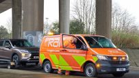 RAC breakdown recovery van with an open door, a technician in a high-vis jacket, and a car being towed.
