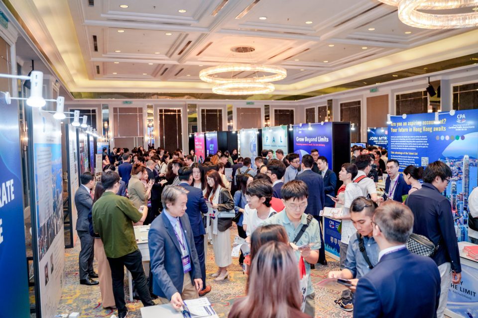Attendees networking at a busy recruitment fair with various company booths and banners