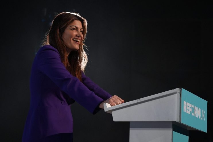 Laila Cunningham of Reform UK smiling while standing at a podium with the partys logo, speaking at an event