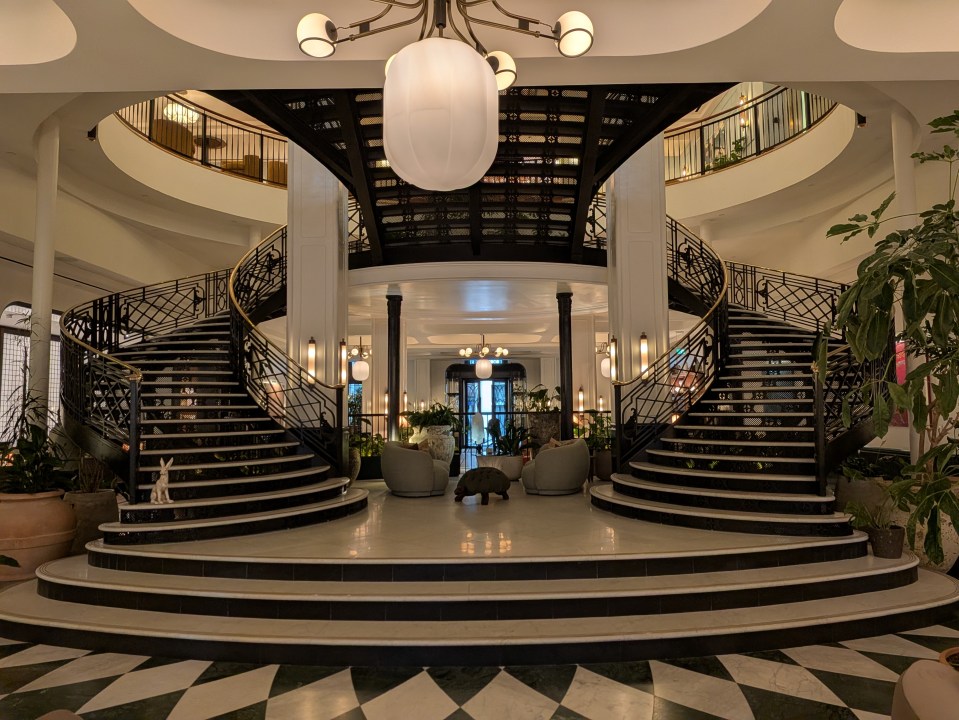 Grand entrance with twin winding staircases and ornate black railings at Six Senses London hotel.